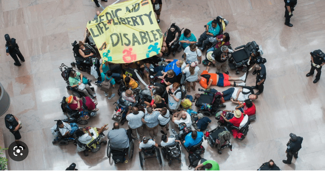A group of people with disabilities gather in the rotunda of the capitol building, holding a banner that says "Medicaid = Life + Liberty 4 Disabled"