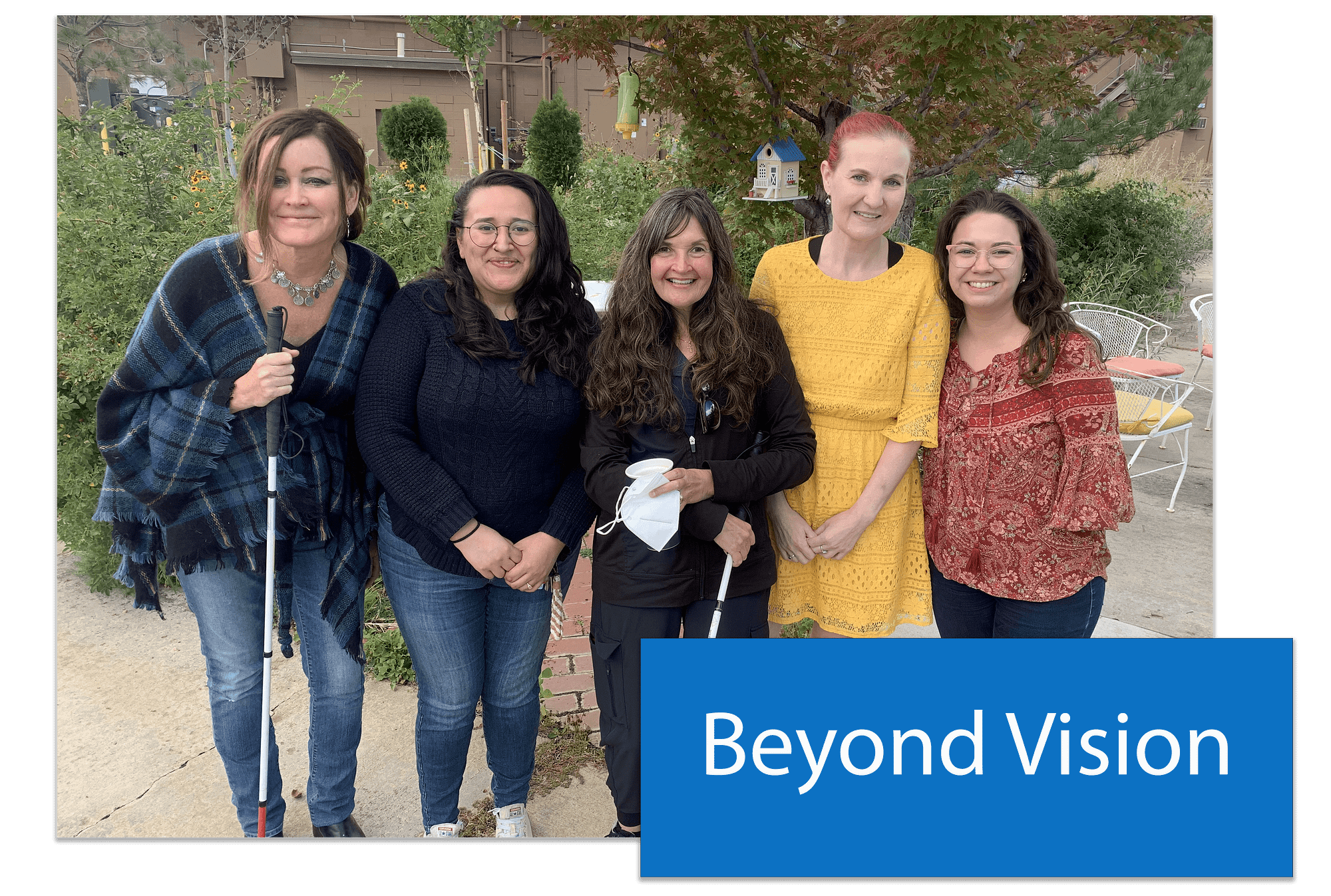 A button that says Beyond Vision placed in the lower right hand corner of an image of a group of five woman. They are the staff of the Beyond Vision program. Two of the women carry walking canes for the visually impaired.