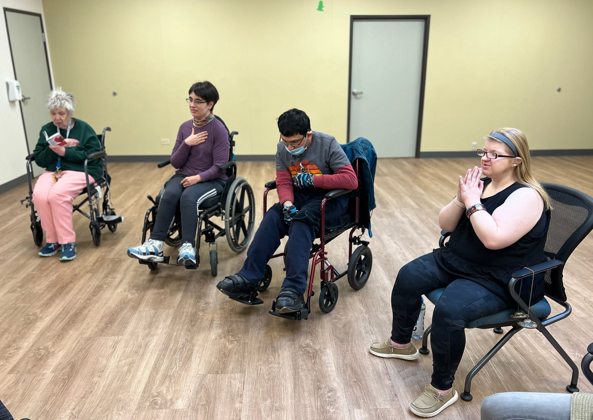 A CPWD Peer Support Group practices yoga. Four poeple are pictured. The three on the left are in wheelchairs, the woman on the right is seated in a chair.