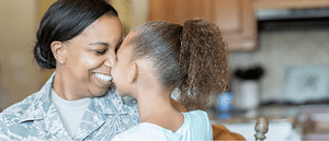 A woman is smiling, nose to nose with her daughter. She is wearing military fatigues. They are both African American.