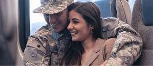 Image description: A man wearing military fatigues hugs a woman as they smile.