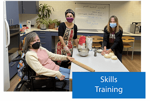 Three women are in a kitchen around a table. The woman on the far left is in a wheelchair and is holding a rolling pin. The woman in the middle has a bowl filled with flour in front of her. The woman on the right is rolling dough. The label in the lower right corner says Skills Training.