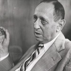 Dr Leo Kanner. Image description: Leo Kanner is pictured in this black and white image wearing a suit jacket and tie. His dark hair is short. He is turned 1/4 turn away from the camera and looks as though he is speaking. His hand is raised next to his face as if gesturing.