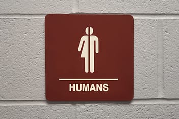 A bathroom sign that has both the male and female icons split in half and put together with the word "Humans" underneath.
