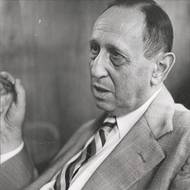 Dr Leo Kanner. Image description: Leo Kanner is pictured in this black and white image wearing a suit jacket and tie. His dark hair is short. He is turned 1/4 turn away from the camera and looks as though he is speaking. His hand is raised next to his face as if gesturing. 